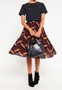 Top corto nero a maniche corte con decorazioni; gonna midi con motivo a zigzag in bordeaux, arancione e blu navy; borsa nera.