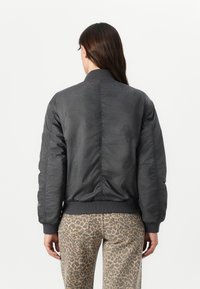 Chaqueta bomber gris con una textura estampada, puños y bajo acanalados, y una silueta clásica, combinada con pantalones de estampado de leopardo.