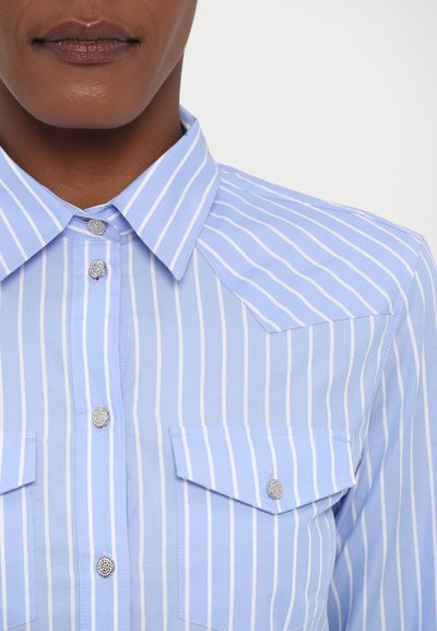 Hellblau gestreiftes Hemd mit Button-Down-Kragen, ausgestattet mit zwei Brusttaschen und dekorativen silbernen Knöpfen auf einem glatten Stoff.