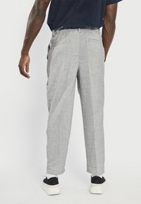 Lys grå bukser med teksturert stoff, elastisk midjebånd og sidelommer, kombinert med svarte sneakers med hvite såler.