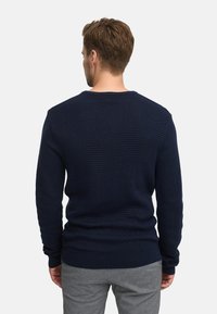 Mørkeblå teksturert genser med rund hals, med ribbestrikkede mansjetter og avslutning, samt diagonale ribbestrikkede mønstre. Glatt materiale.