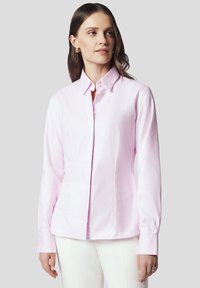 Jasnoróżowa bluzka z długim rękawem, z kołnierzykiem zapinanym na guziki, o dopasowanym fasonie i gładkiej tkaninie. Posiada guziki przy mankietach i szczegóły przy przodzie.