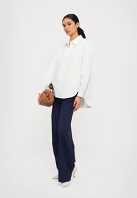 Weißes Hemd mit langen Ärmeln, kombiniert mit marineblauen weit geschnittenen Hosen. Braune strukturierte Handtasche und beige spitze Schuhe.