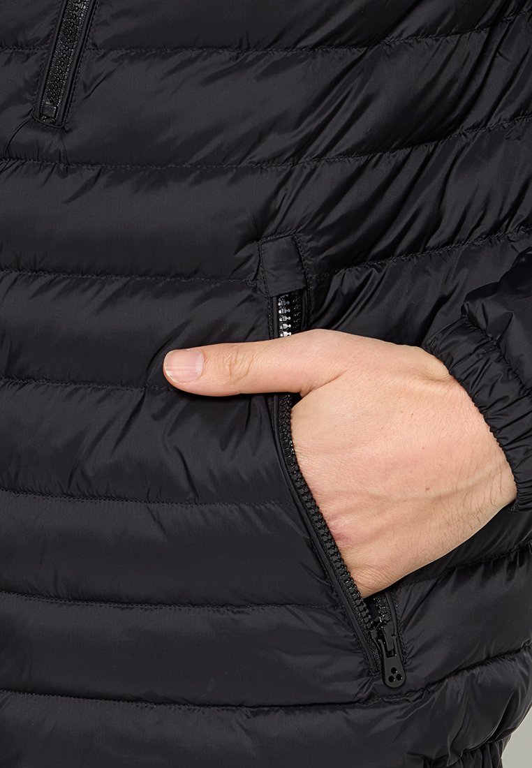 Zwarte pufferjack met horizontale quiltontwerp, een ritszak aan de linkerkant en elastische manchetten. Zacht, lichtgewicht materiaal.