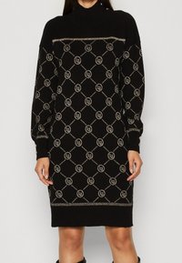 Svart långärmad stickad klänning med metallisk geometrisk mönstring och små logotyper, hög halsringning och knapppdetaljer på manschetterna.