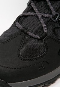 Close-up of black hiking shoe with textured fabric, reinforced toe, and grey braided laces threaded through eyelets.