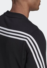 Felpa nera con accenti a doppia striscia bianca lungo le spalle e la parte superiore della schiena, realizzata in un tessuto testurizzato e con un design classico a girocollo.