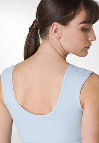 Ljusblå träningslinne med djup rundad rygg, slät textur och smala band som avslöjar hudtonen vid halsringningen och axlarna.