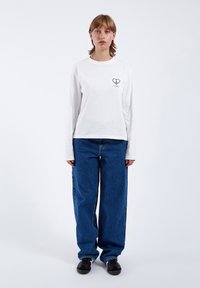 White long-sleeve t-shirt with a black heart graphic on the chest, paired with loose-fit blue denim jeans and black shoes.