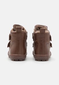 Bottines en cuir marron avec une finition texturée, dotées d'une doublure intérieure duveteuse, de deux sangles velcro et d'une semelle robuste.