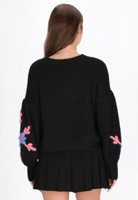 Czarny sweter dzianinowy z oversized'owymi rękawami, ozdobiony kolorowym haftem kwiatowym w odcieniach różu i niebieskiego. Miękka struktura oraz luźny krój.