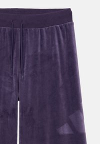 Purple velour joggers with an elastic waistband, drawstring, and smooth texture. Features a subtle logo on the lower leg in a matte finish.