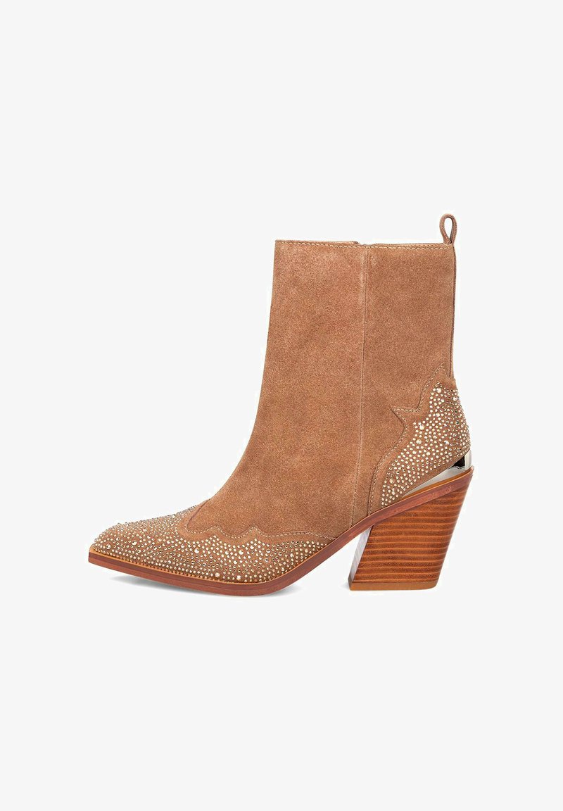 Botín de ante marrón claro con punta afilada, diseño de ondas decorativas, adornos con tachuelas y un tacón de madera apilada.