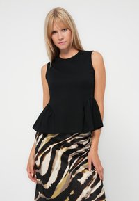 Black sleeveless top with peplum hem, made from smooth fabric. Worn with a patterned skirt featuring bold stripes in black, white, and brown tones.