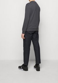 Mörkgrå sweatshirt med lång ärm, rund halsringning och ribbade mudd, tillsammans med mörka jeans och svarta träningsskor.