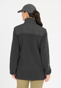 Harmaa fleece-takki korkealla kauluksella ja sileällä yläosalla. Omaavat pitkät hihat ja rento istuvuus. Yhdistettynä yhteensopivaan harmaaseen lippalakkiin.