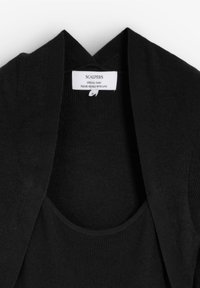 Chaleco de punto negro con abertura frontal, textura acanalada y solapas anchas. Incluye una etiqueta de cuidado en el interior con el nombre de la marca y la talla.