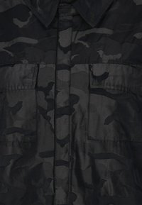 Sort camouflage skjorte med knap-åndet krave, to brystlommer og en glat, letvægts stofstruktur.
