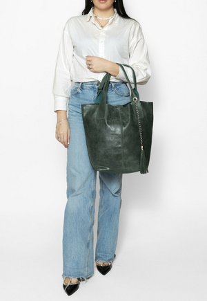 Sac fourre-tout en cuir vert avec deux anses d'épaule, orné d'un accent chaîne et d'un détail pompon, présenté sur un fond neutre.