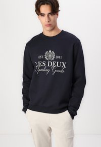 Sudadera de algodón azul marino con cuello redondo, con texto impreso en blanco "LES DEUX Sporting Goods" y el año de fundación, con puños y dobladillo acanalados.