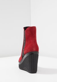 Czerwona zamszowa botka na koturnie, z teksturowaną czarną platformą i bocznym zamkiem błyskawicznym z wytłoczonym napisem „Calvin Klein Jeans”.
