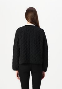 Sort quiltet jakke med en kasseformet pasform, rund halsudskæring og struktureret mønster. Lange ærmer og minimal detaljer fuldender designet.