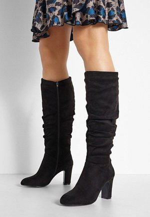 Bottes noires en daim au-dessus du genou avec un design décontracté, un talon haut et un zip sur le côté. Texture lisse et style minimaliste.