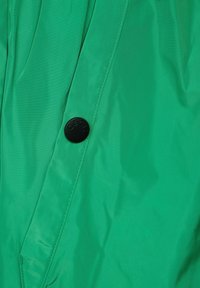 Giacca a vento verde realizzata in tessuto liscio e leggero, dotata di chiusura a bottoni neri con marchio "CECIL" e una texture leggermente sgualcita.