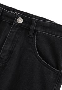 Un pantalon en denim noir présente un tissu texturé, une fermeture à bouton argenté et des poches avant. Le design est classique avec des ouvertures de jambe droites.