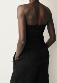 Top strapless nero con design aderente, abbinato a pantaloni cargo neri larghi con tasche e tessuto texturizzato.