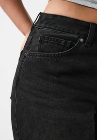 Jeans de mezclilla negra con una cintura alta, bolsillos laterales y detalles de costura sutiles. La tela tiene un acabado suave y texturizado.