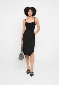 Fekete testhezálló ruha négyzet alakú nyakkivágással, díszes övcsattal. Fekete hegyes orrú magassarkúval és texturált kézitáskával párosítva.