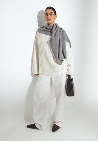 Chunky white cable-knit sweater, gray scarf draped over shoulders, wide white trousers, black handbag, and pointed black flats.
