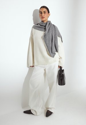 Chunky white cable-knit sweater, gray scarf draped over shoulders, wide white trousers, black handbag, and pointed black flats.