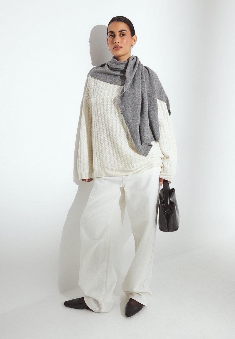 Chunky white cable-knit sweater, gray scarf draped over shoulders, wide white trousers, black handbag, and pointed black flats.