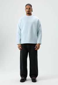 Sweat-shirt bleu clair à encolure ronde et manches longues, associé à un jean noir ample et des chaussures noires épaisses avec des lacets roses.