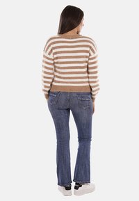 Maglione a righe beige e bianco con texture pelosa, abbinato a jeans a zampa d'elefante blu. Sneakers bianche completano l'outfit.