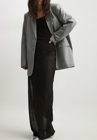 Harmaa ylisuurikokoinen bleiseri, musta läpikuultava hame, musta toppi alla, kerroksittainen muotoilu, kevyt kangas ja hopeiset tennarit.