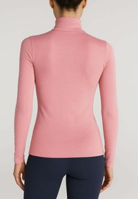 Maglietta a maniche lunghe con collo alto in morbido tessuto rosa, design aderente, texture liscia, con uno stile minimalista e senza motivi o accessori visibili.