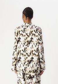 Blusa ampia con un motivo animalier tenue in beige, nero e oliva su tessuto liscio; presenta un colletto a punta e maniche lunghe.