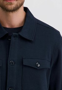 Marineblauwe overhemd met knopen en een kraag, twee borstzakken en zwarte knopen. Gemaakt van een soepele, gestructureerde stof. Korte mouwdetails zichtbaar.