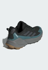 Schwarzer und türkisfarbener Sportschuh mit strukturiertem Obermaterial, verstärktem Fersenbereich, grauem Zwischensohlenelement und robustem Gummilaufsohle. Enthält Schnürsenkel und Zuglasche.