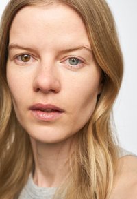 Närbild av ett ansikte med medellång blont hår. Drag inkluderar blå och bruna ögon, naturlig hudstruktur och en neutral läppfärg.