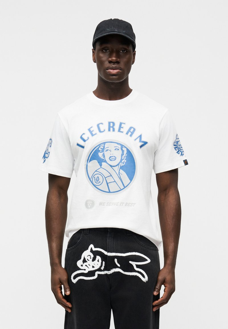 Λευκό μπλουζάκι με μπλε γραφικό τύπωμα μιας γυναίκας και το κείμενο "ICECREAM" από πάνω. Μαύρο παντελόνι με λευκό καλλιτεχνικό σχέδιο σκύλου στο πίσω μέρος.