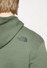 Felpa verde oliva con cappuccio. Presenta polsini e orlo a coste. Logo stampato in nero sulla spalla sinistra. Tessuto morbido e strutturato.