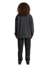 Schwarze, wasserfeste Jacke mit lockerer Passform und hohem Kragen. Schwarze Hose mit einem dezenten Muster und gestickter Nummer 223 am Bein.