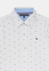 Biała koszula zapinana na guziki z małym, powtarzającym się niebieskim wzorem w kwadraty. Posiada jasnoniebieski kołnierzyk oraz logo Tommy Hilfiger na piersi.