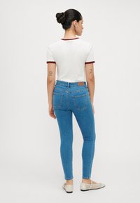 Λευκό μπλουζάκι με μπορντό λεπτομέρειες συνδυασμένο με μπλε τζιν παντελόνι skinny. Το τζιν διαθέτει πίσω τσέπες και καφέ δερμάτινη ετικέτα πάνω από την κοιλιά.