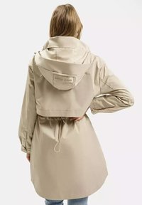 Beżowa kurtka wodoodporna z kapturem, ściągaczem w talii i mankietami na guziki; na górnej części pleców znajduje się logo "CROSS JEANS".