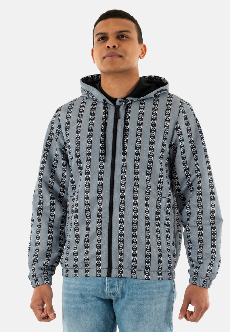 Chaqueta ligera con capucha de tela gris, que presenta atrevidos logotipos negros en franjas verticales. Con cremallera en la parte delantera y puños elásticos.